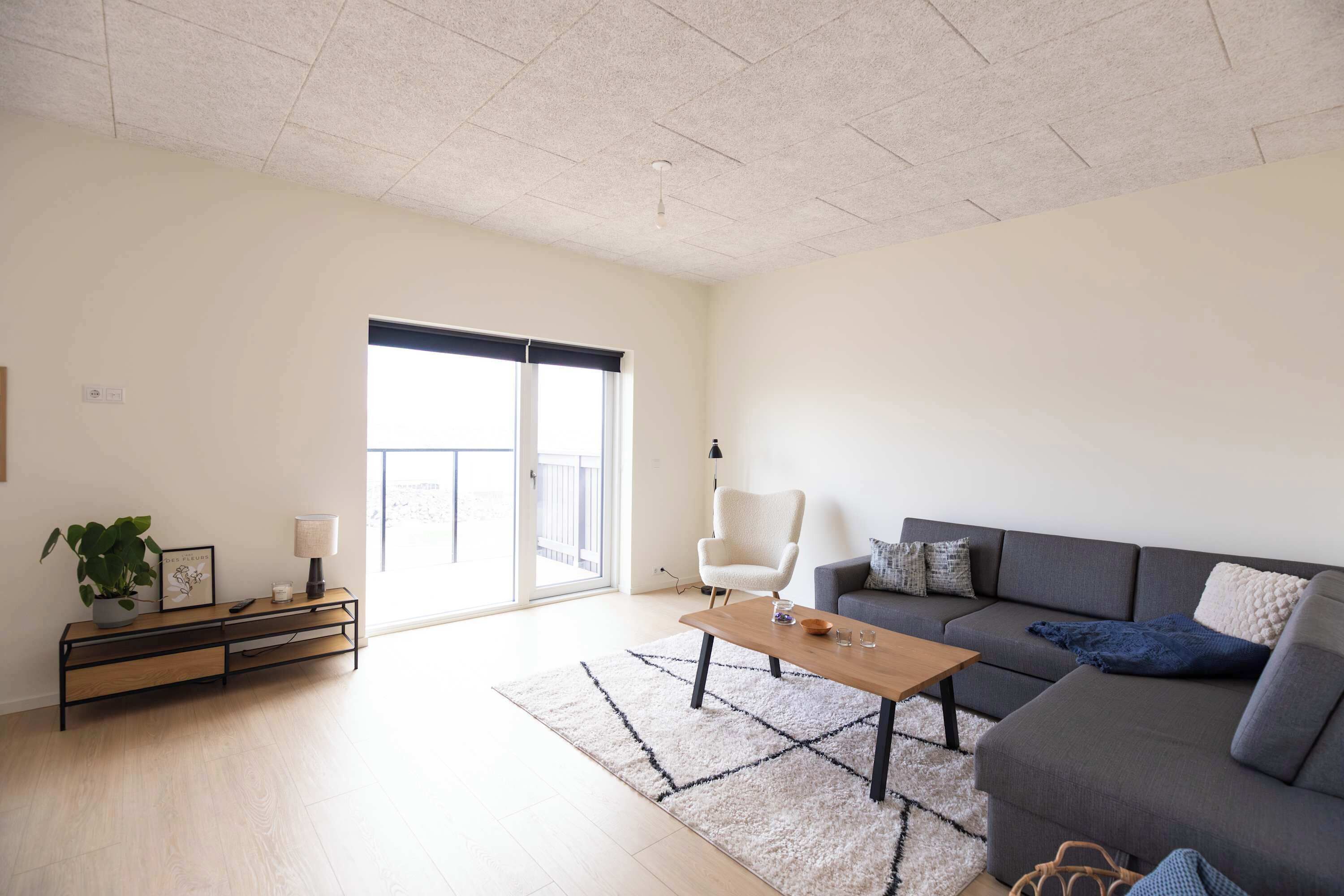 Un salon moderne avec un canapé gris, une table basse en bois et un fauteuil blanc.