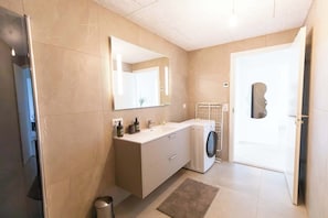 Een moderne badkamer met een grote spiegel, een ingebouwde wasmachine en een toilet.