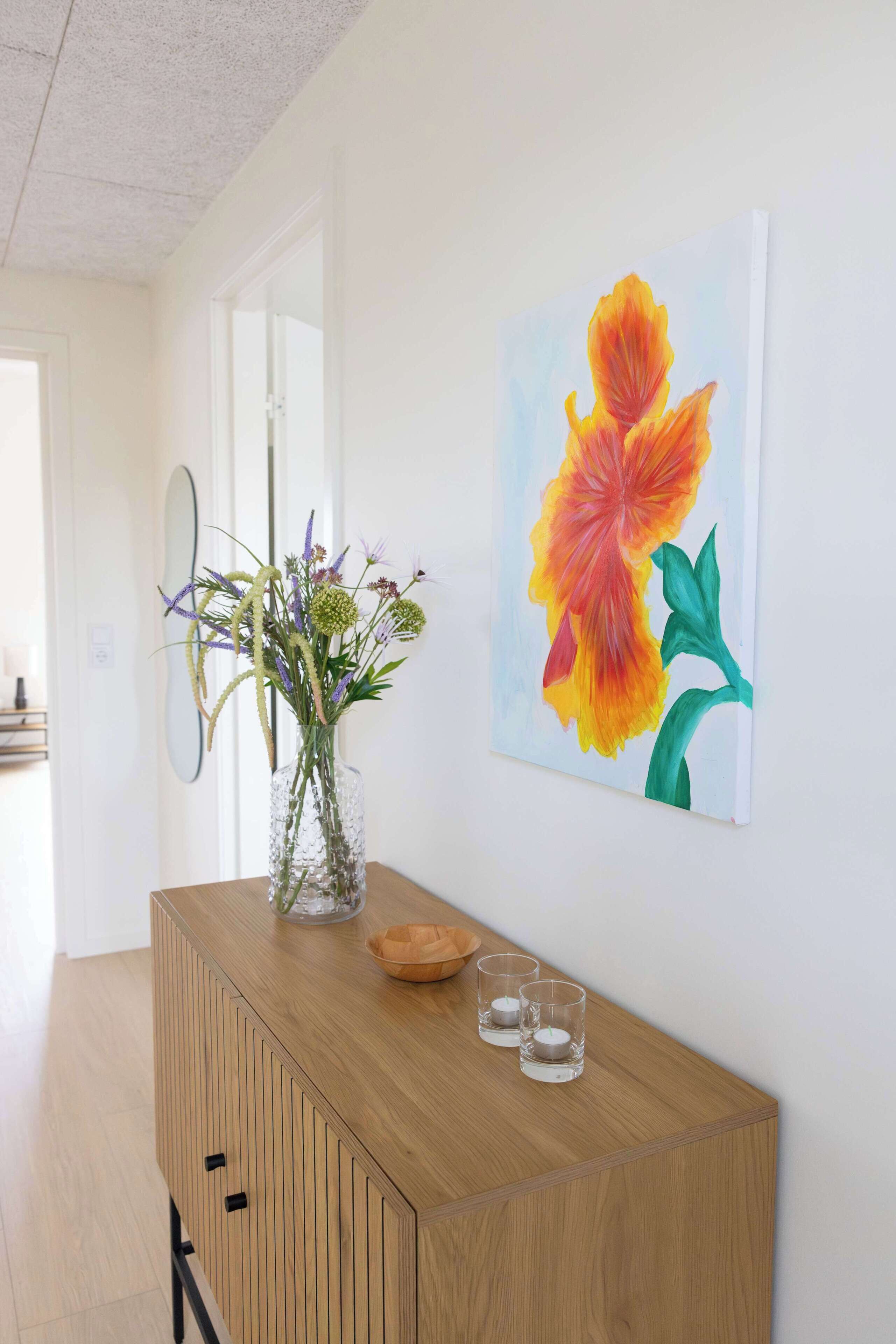 Een gang met een houten console tafel, een vaas met bloemen en een bloemstillevaan aan de muur.