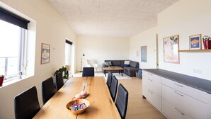 En moderne stue med spiseplads, med en sofa, et spisebord med stole og et køkkenområde med skabe.