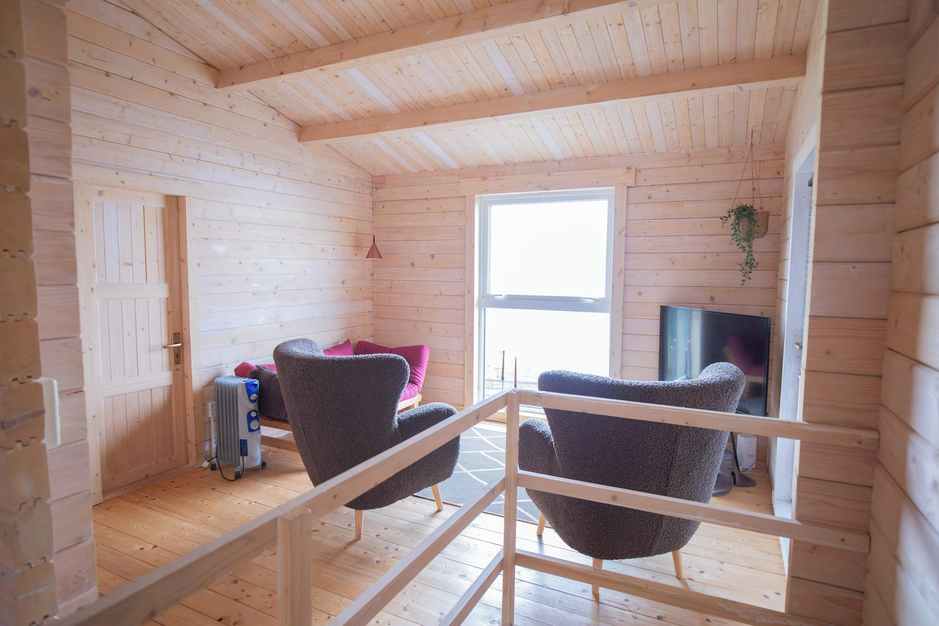 A wooden cabin interior with a high ceiling, a large window, and a seating area with two chairs.