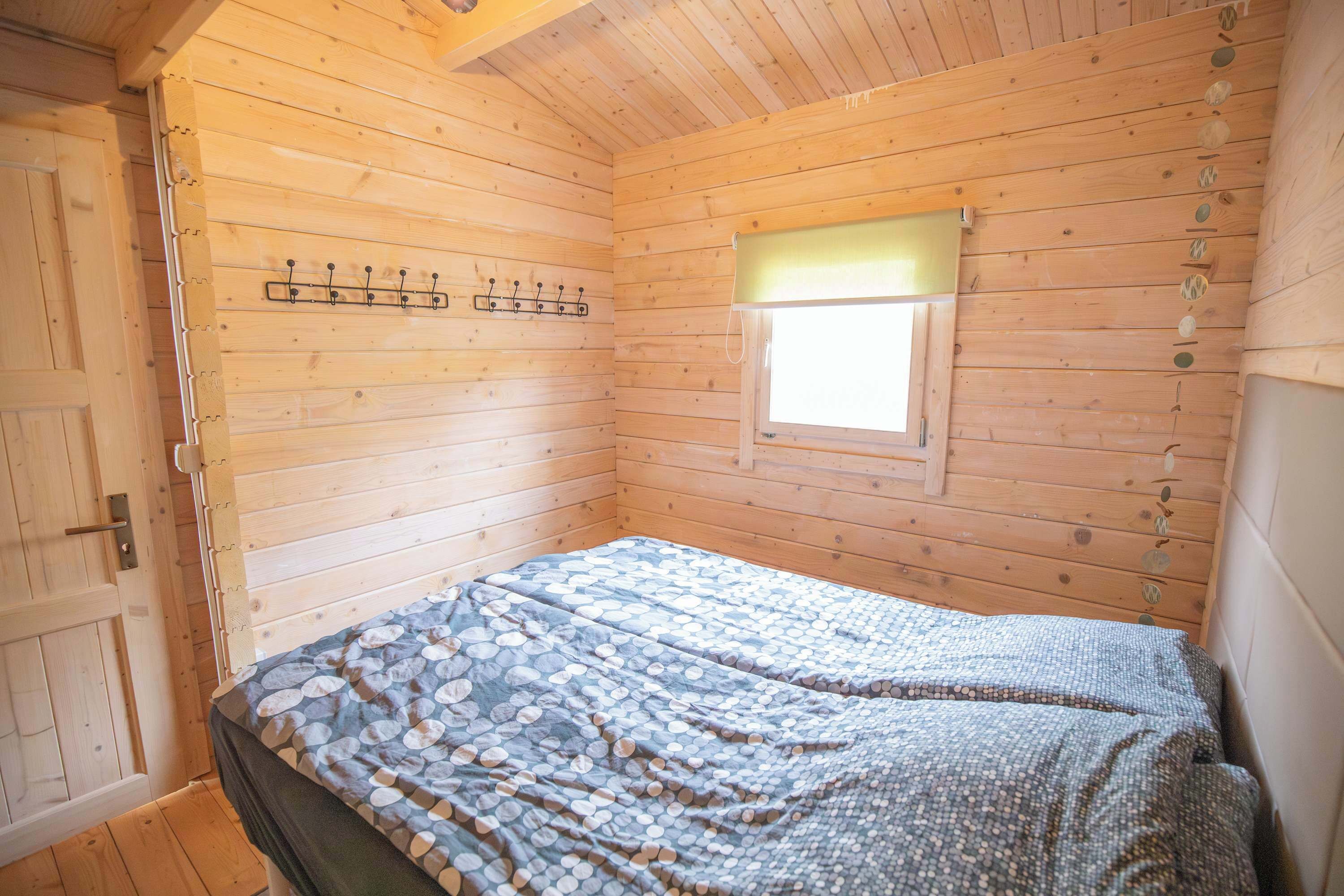 Een kamer met een houten vloer, een bed, een raam en een kapstok.