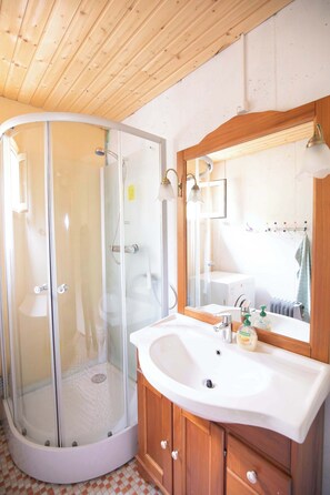 Une salle de bain avec une douche à parois de verre, un lavabo blanc avec un meuble en bois et un miroir agrémenté de luminaires fixés au mur.