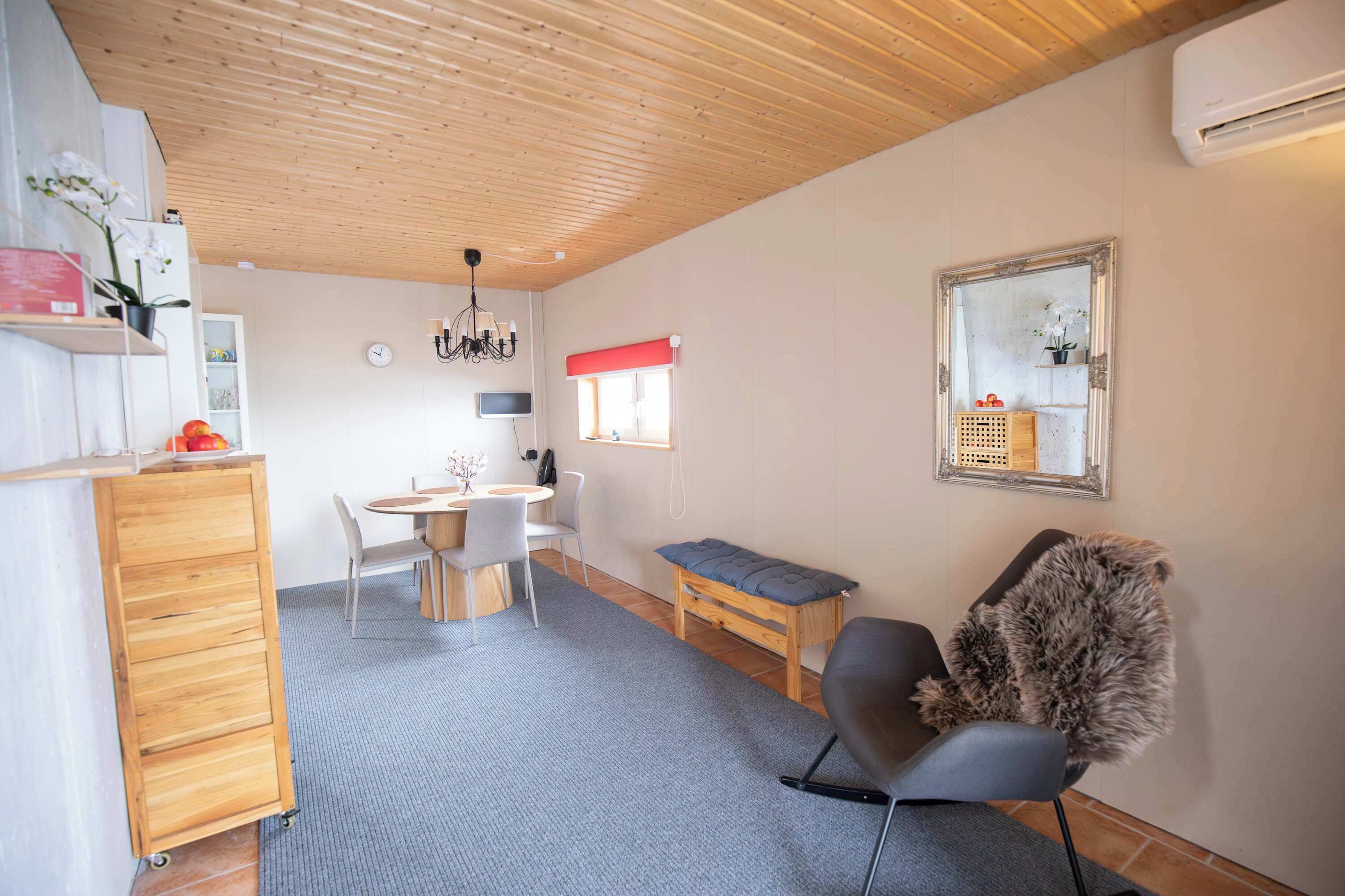 Un espace de vie compact comprenant un coin cuisine, un coin repas, un espace détente avec un banc et un grand miroir.