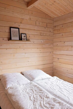 Une pièce aux murs recouverts de lambris en bois, un lit avec une literie blanche et deux tableaux encadrés posés sur une étagère.