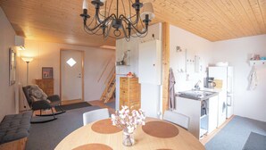 Una sala de estar acogedora con techo de madera, una mesa de comedor con un jarrón de flores y una cocina con refrigerador y cafetera.