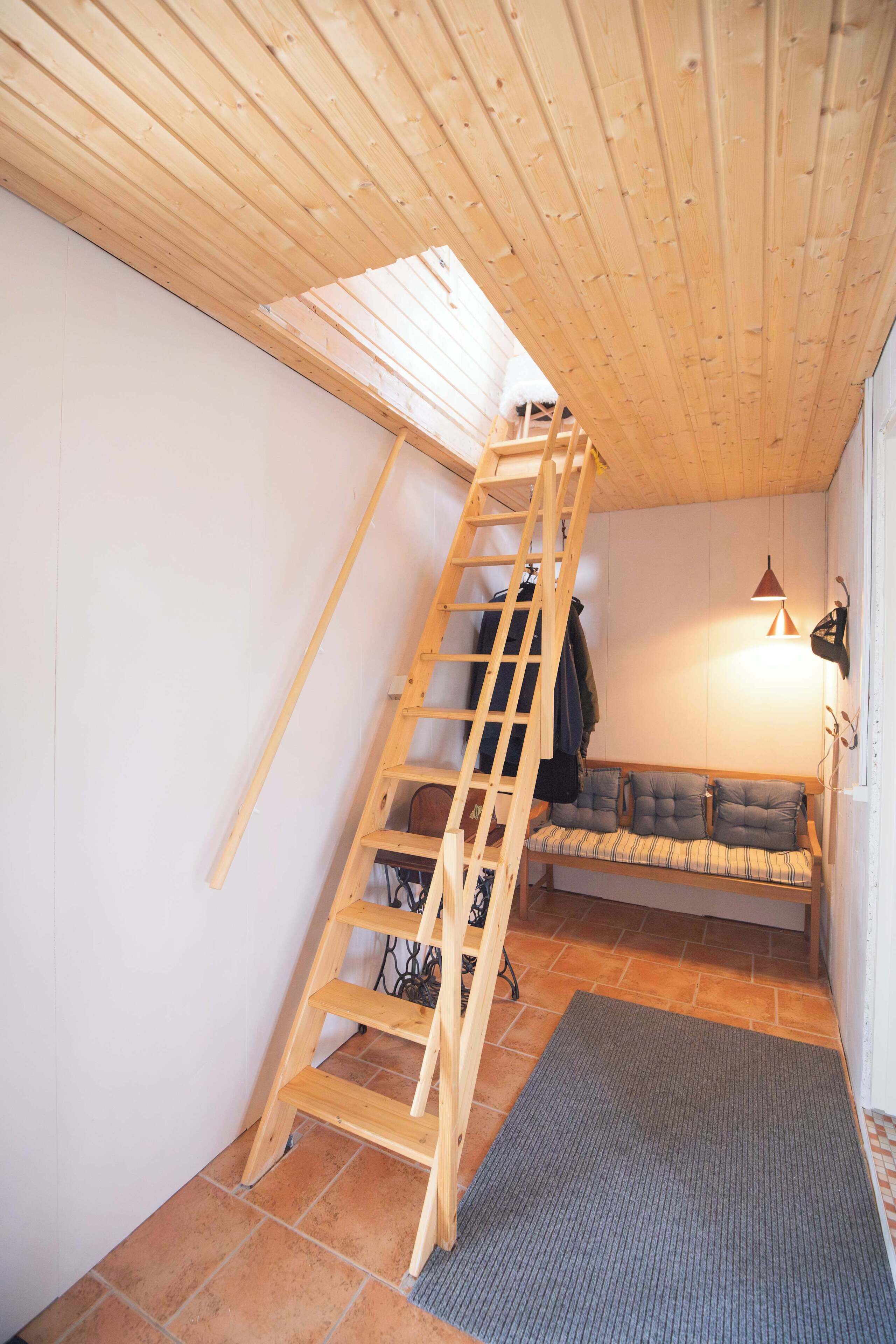 Une chambre à coucher aménagée dans les combles, avec un escalier en bois, un banc avec des coussins et un plancher carrelé.