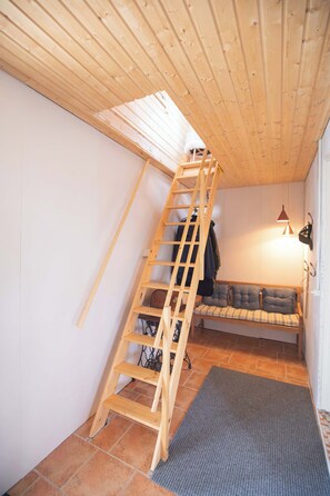 A wooden loft bedroom with a wooden ladder, a bench with cushions, and a tiled floor. - Scenic Villa Cabin by the Sea in Faroe Islands (Innan Glyvur)