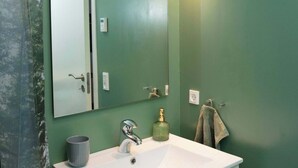 Une salle de bain avec un lavabo blanc, un miroir, une serviette et un mur vert.