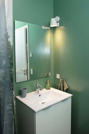 A bathroom with a white sink, a mirror, a towel, and a green wall. - Cozy & Characterful Faroese Apartment - 2 Bedrooms (Tórshavn)