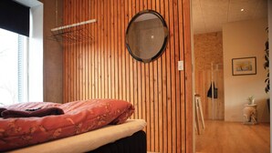 Une chambre à coucher avec un lit, un mur recouvert de lambris en bois, un miroir rond et une porte donnant sur une autre pièce.