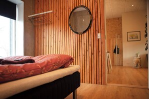 A bedroom with a bed, a wooden slat wall, a round mirror, and a door leading to another room. - Cozy & Characterful Faroese Apartment - 2 Bedrooms (Tórshavn)