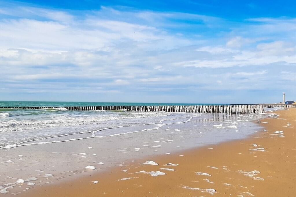 A beach with a wooden pier extending into the water, a clear sky, and a calm sea.