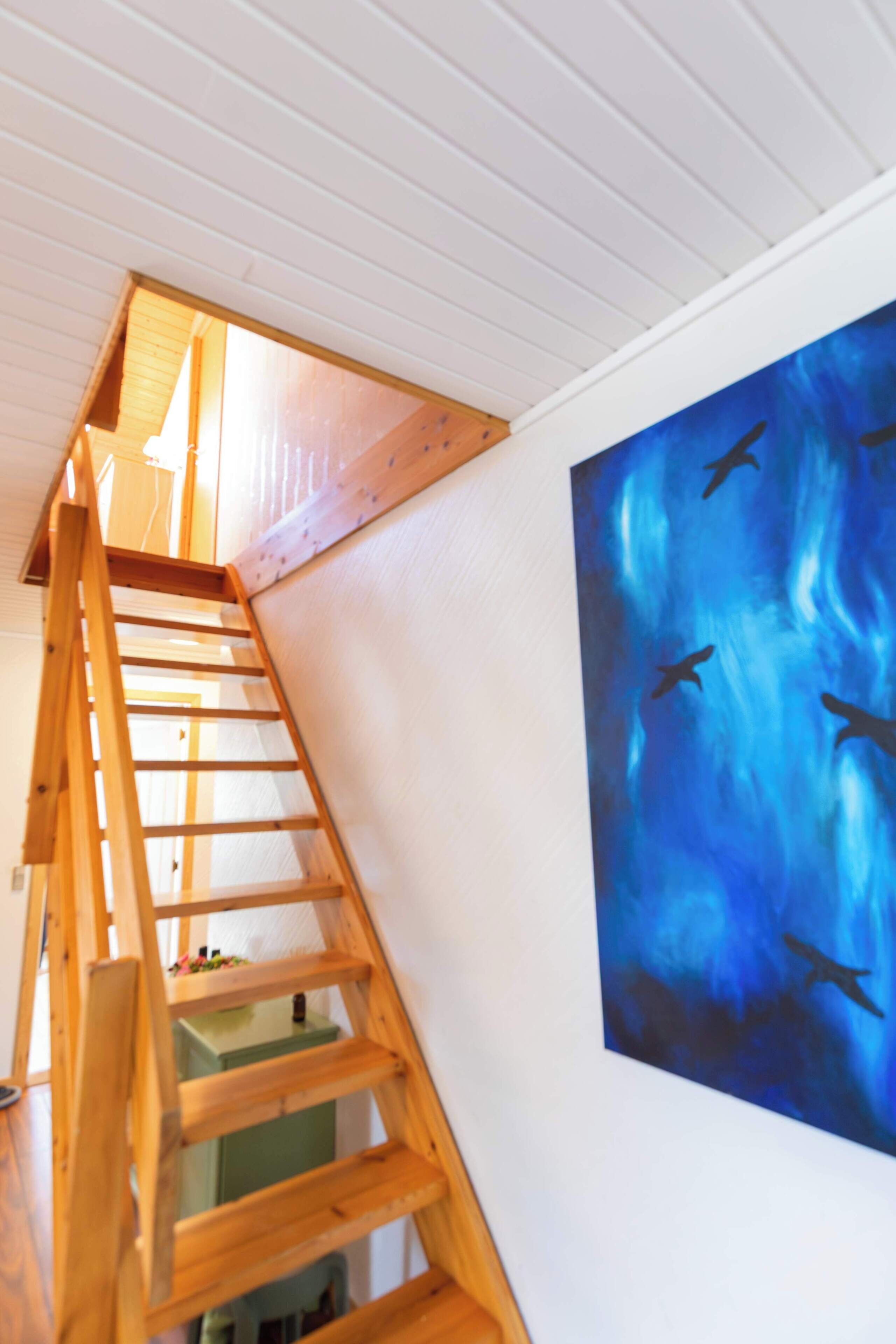 Una scala in legno conduce a un piano superiore, con un dipinto blu raffigurante uccelli sulla parete.