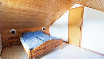 A single wooden bed in a room with a sloped ceiling, a small bedside table, and a door.