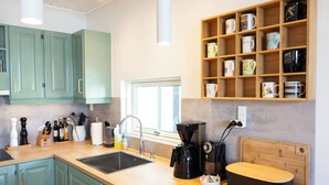 A modern kitchen with teal cabinets, a coffee machine, and a variety of mugs on shelves.