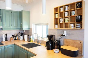 A modern kitchen with teal cabinets, a coffee machine, and a variety of mugs on shelves.