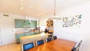 Une cuisine moderne avec des armoires de couleur turquoise, un îlot central en bois et un coin repas comprenant une table et des chaises en bois.