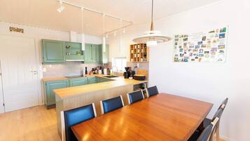 Una cucina moderna con mobili color petrolio, un'isola in legno e un'area pranzo con tavolo e sedie in legno.