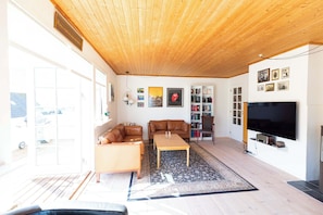 A living room with a wooden ceiling, a sofa, a coffee table, a bookshelf, and a television.