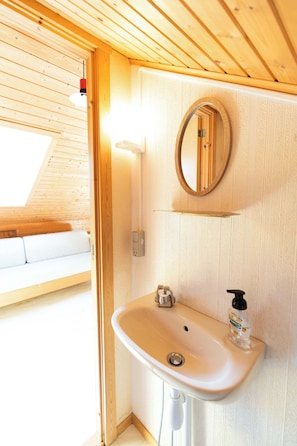 A wooden interior with a white sink, a mirror, and a bottle of hand sanitizer.