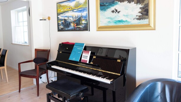 Un piano avec des partitions, une chaise et deux tableaux accrochés au mur.