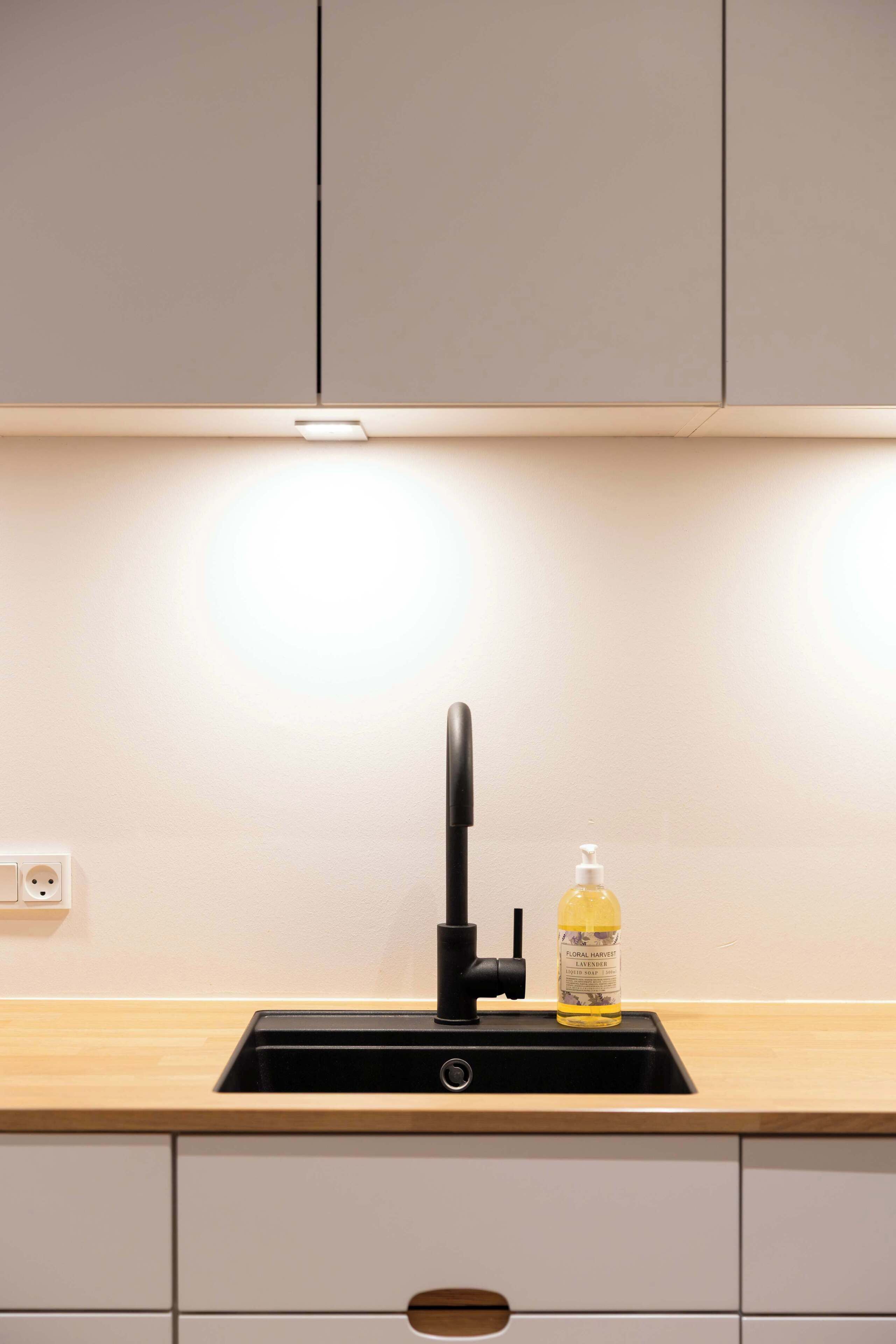 Une cuisine avec un robinet noir, un flacon de savon liquide et un plan de travail en bois.