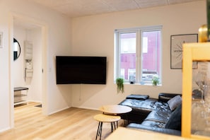 A modern living room with a black leather sofa, a small round table, and a flat-screen TV mounted on the wall.