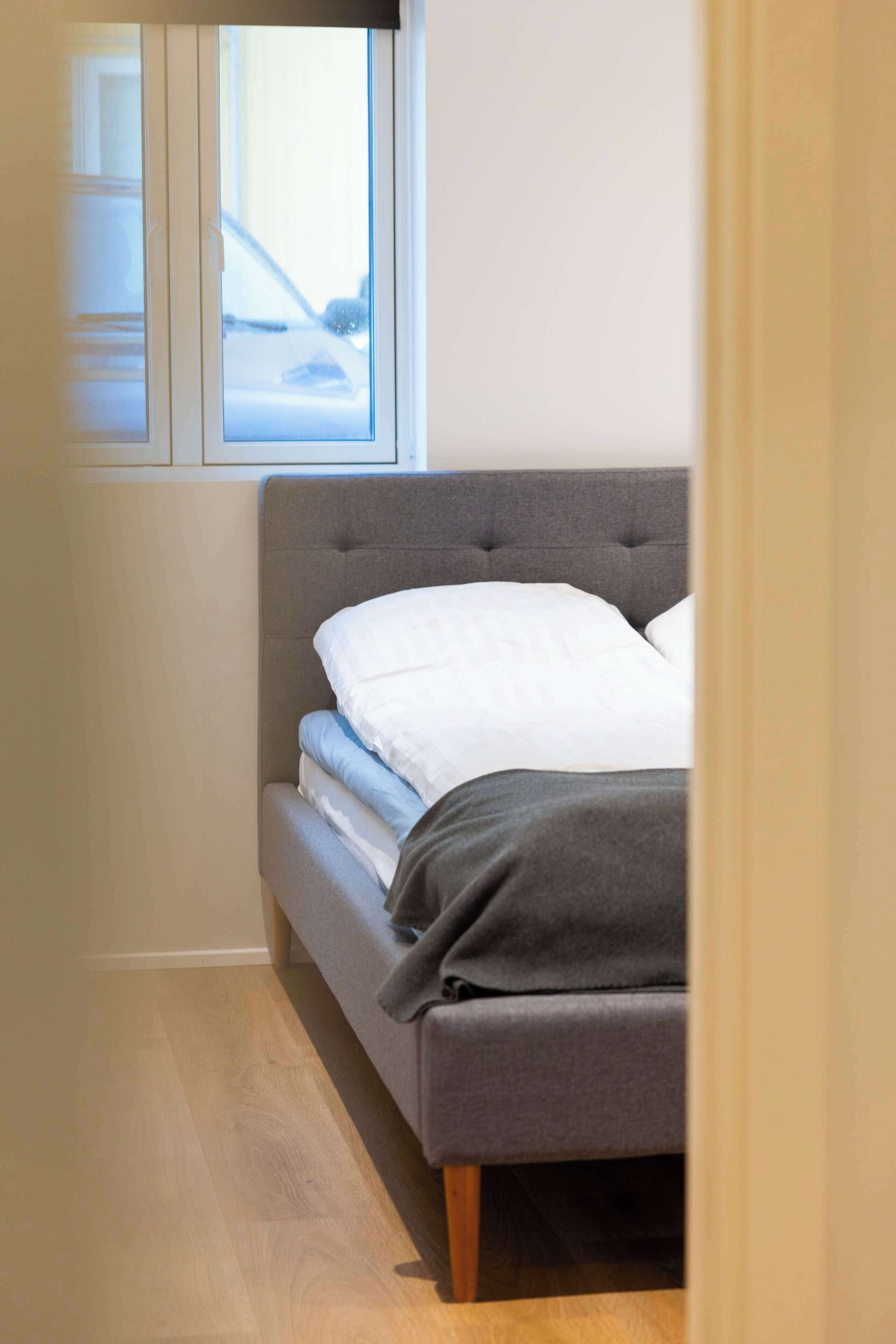 A bedroom with a bed, a window, and a wooden floor.