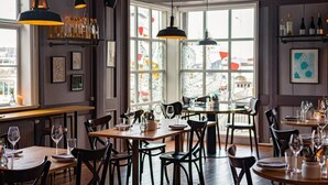 Een restaurantinterieur met meerdere eettafels, stoelen, hangende吊灯 en een uitzicht door grote ramen.