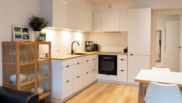 Een moderne keuken met witte kasten, een inbouwoven en een eethoek met een witte tafel en stoelen.