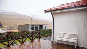 Une terrasse en bois avec un banc, un bâtiment doté d’un toit rouge et un paysage montagneux en arrière-plan.