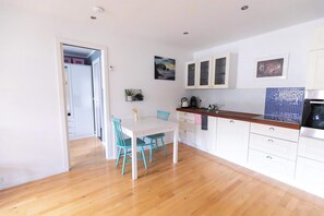 Una cocina compacta con armarios blancos, encimera de madera y comedor con mesa blanca y sillas turquesas.
