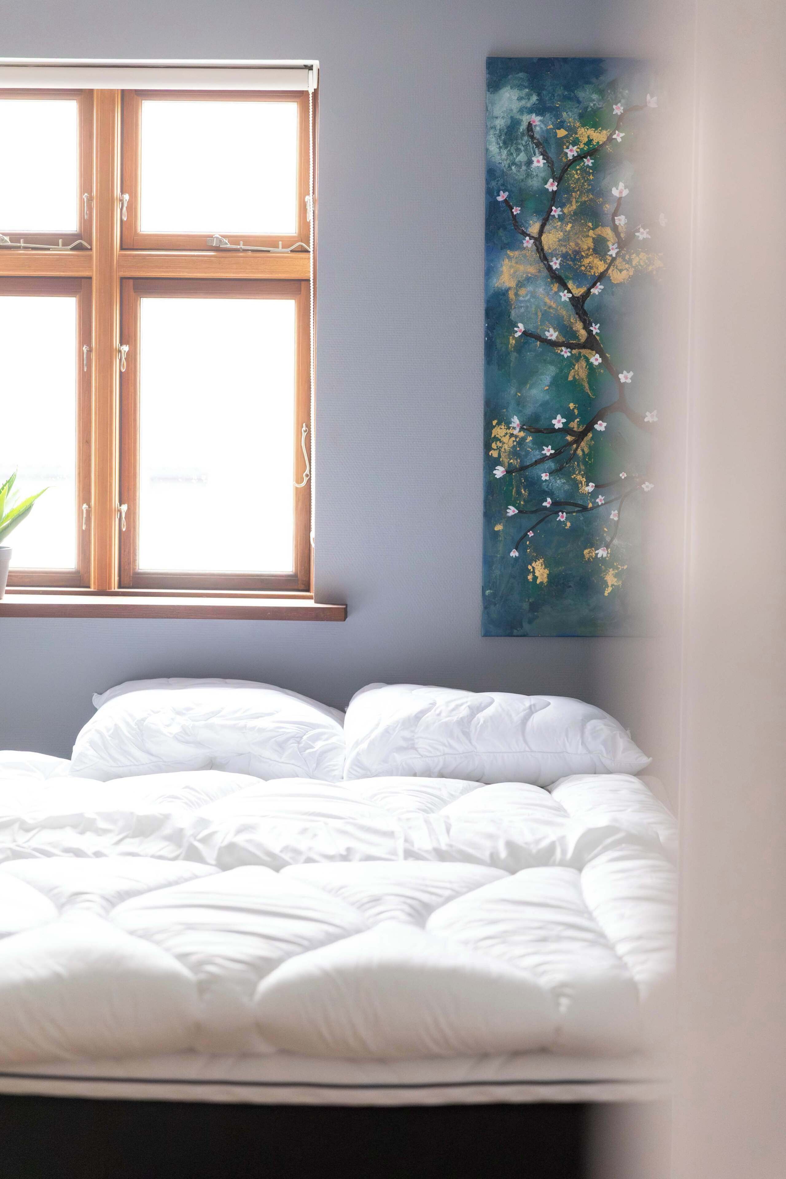 A bedroom with a bed, a window, and a wall-mounted painting.