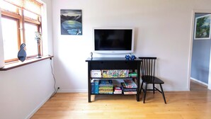 Une pièce avec un téléviseur posé sur un meuble noir, une bibliothèque remplie de DVD, une chaise et une fenêtre avec des rideaux.