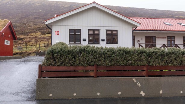 A white building with the number 10, a red roof, and a wooden fence in front. - A serene escape in scenic surroundings (Streymnes)