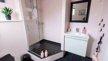 A bathroom with a glass shower enclosure, a white sink with a mirror above it, and a black tiled floor.