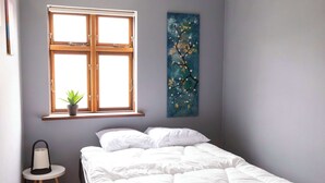 Une chambre avec un lit, une fenêtre avec une plante et un tableau accroché au mur.