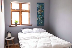 Un dormitorio con cama, una ventana con planta y un cuadro en la pared.