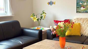 A living room with a black leather sofa, a coffee table, a vase with flowers, and a painting on the wall.