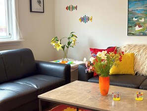 A living room with a black leather sofa, a coffee table, a vase with flowers, and a painting on the wall.