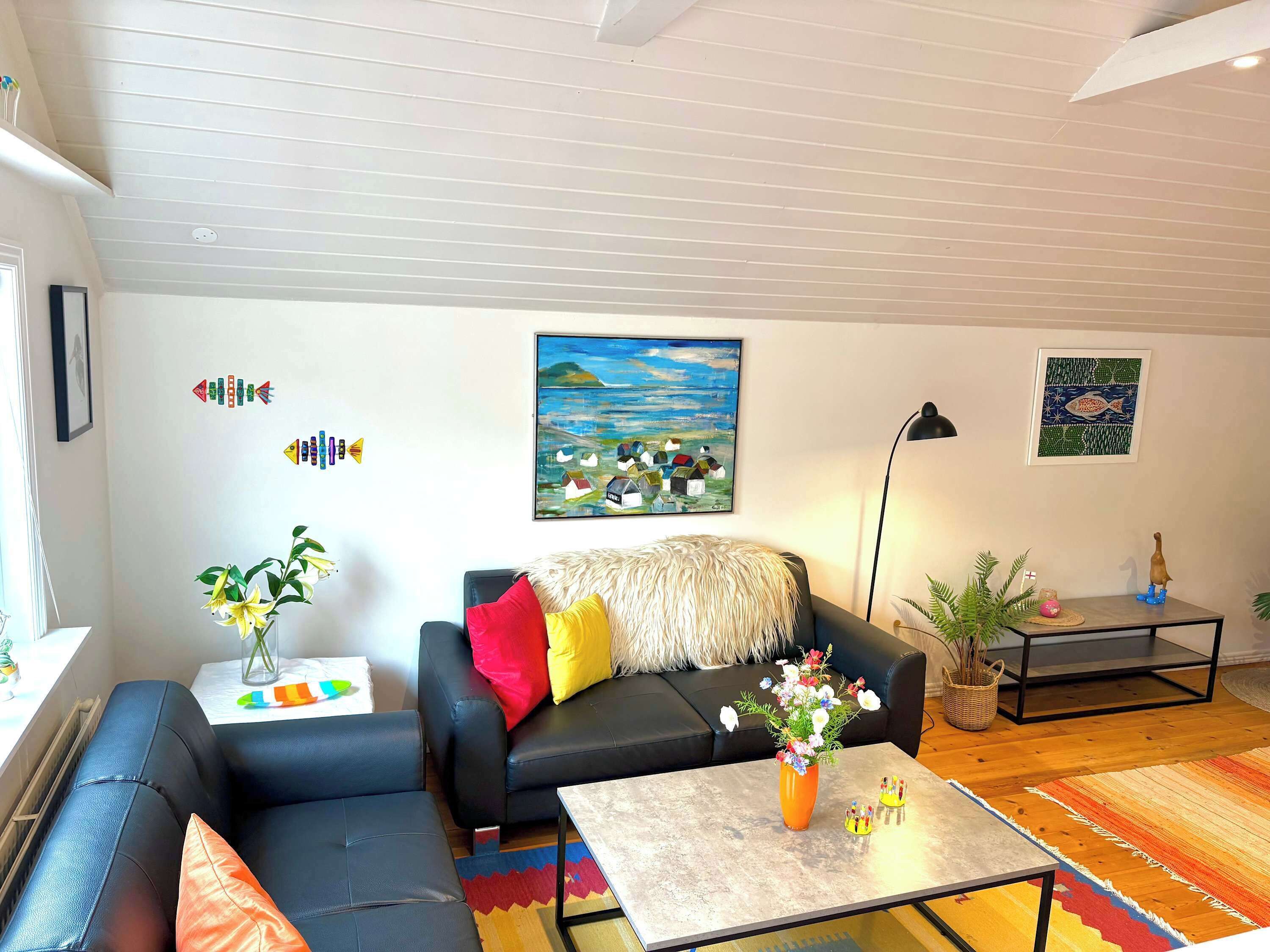 Ein Wohnzimmer mit einem schwarzen Sofa, einem Couchtisch, einem Bild an der Wand und einer Lampe.