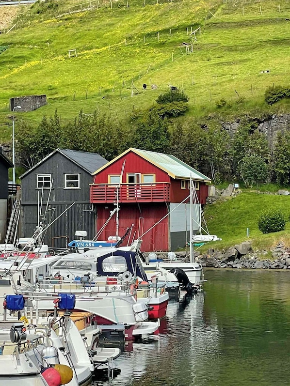 Een jachthaven met aangemeerde boten, een rood gebouw met balkon en een grasheuvel op de achtergrond.