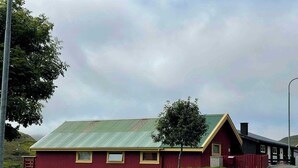 A red building with a green roof, a small window, and a door. - Harbourfront Boathouse Vestmanna Bird Cliffs (Vestmanna)