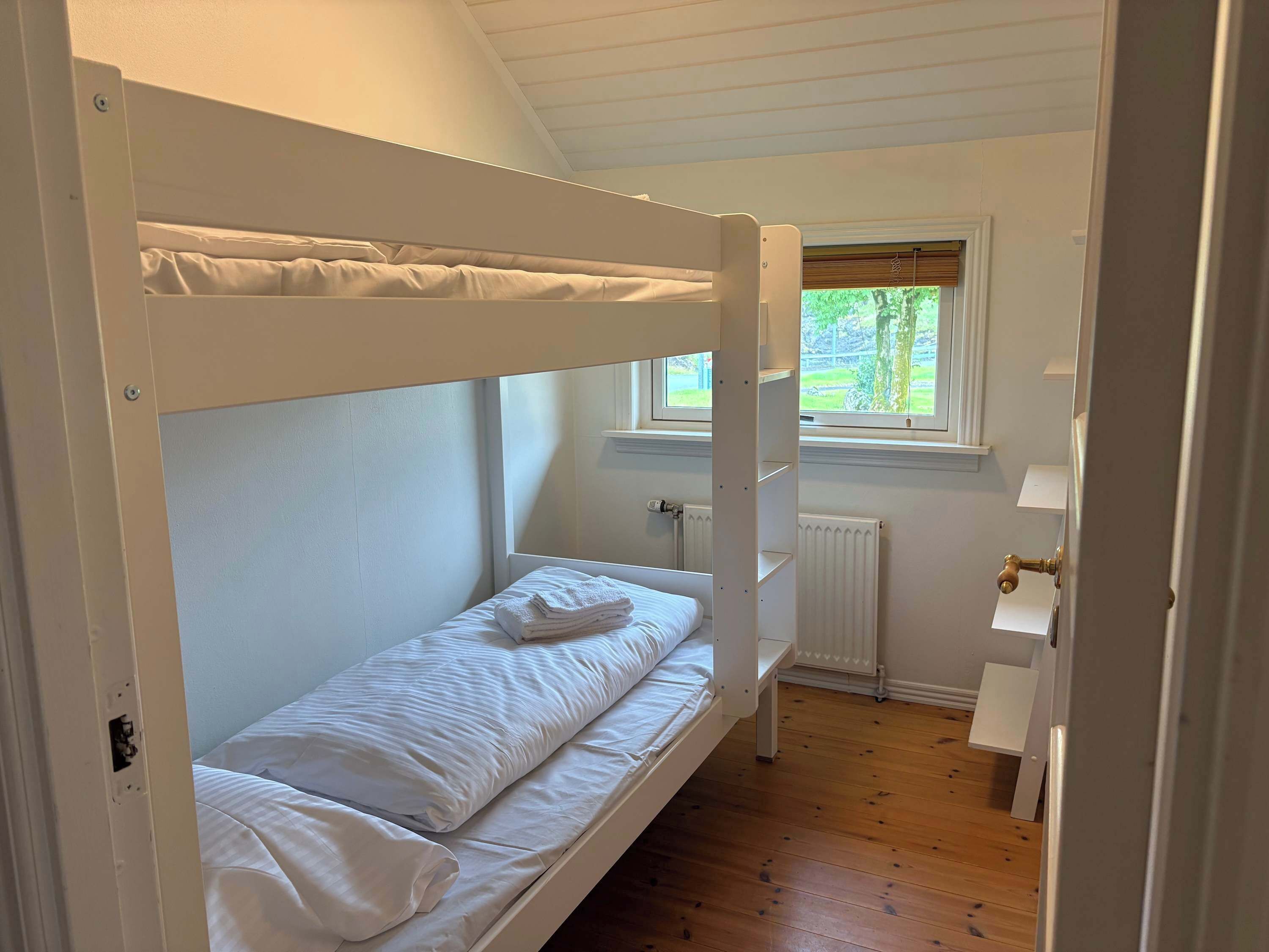 A bunk bed in a room with a window, a radiator, and a door.
