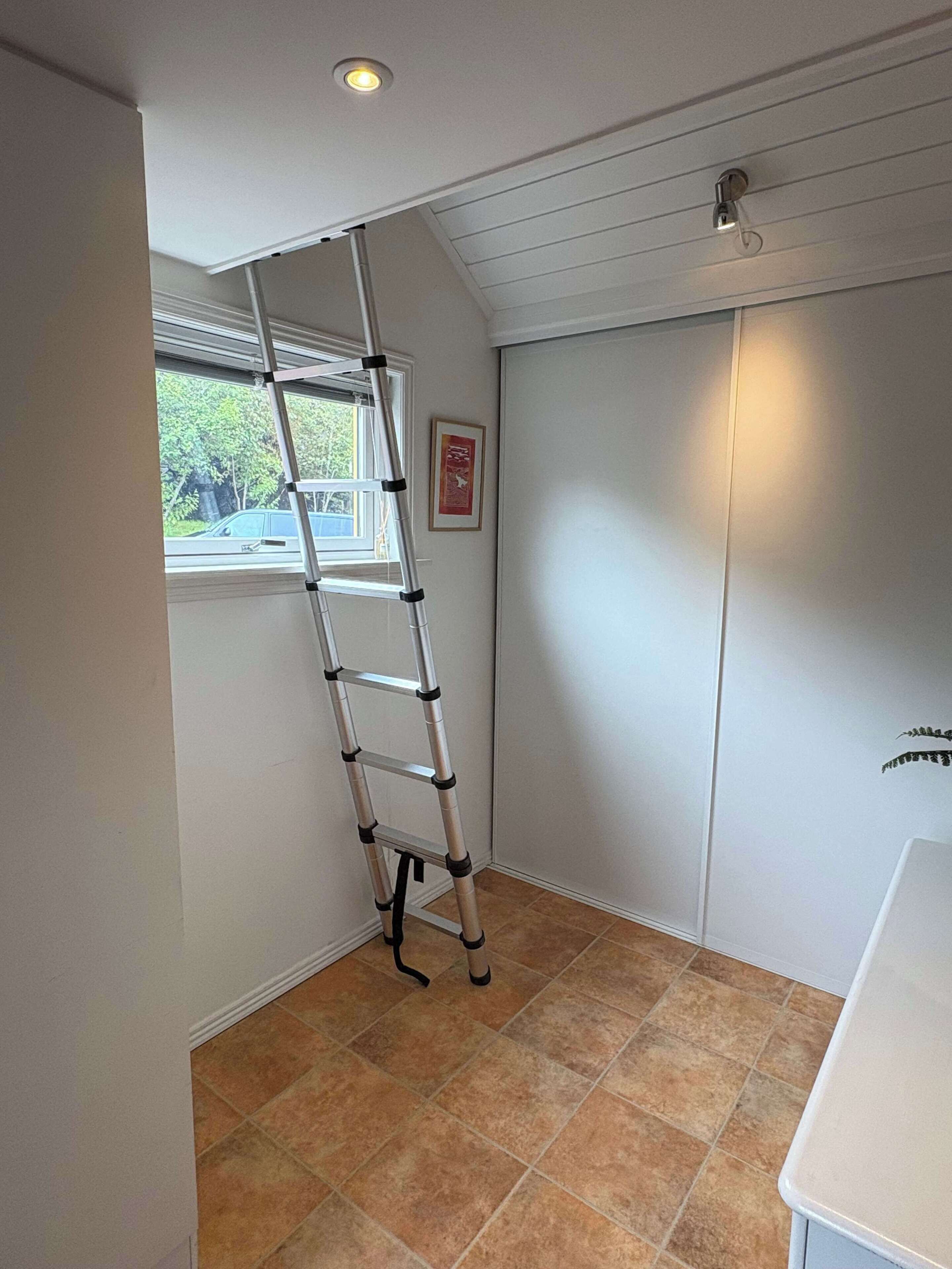 Een kamer met een witte muur, een raam, een ingelijste foto, een witte deur en een betegelde vloer.