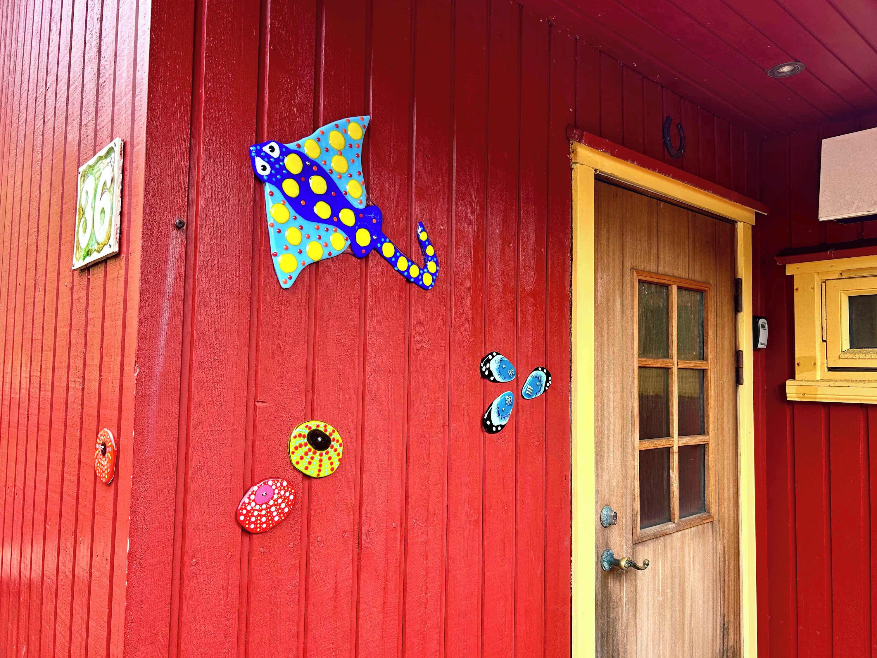 En röd trädörr med ett fönster, en gul list och ett mässingshandtag.