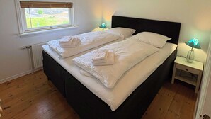 A bedroom with a large bed, a window, a radiator, a ceiling light, and a bedside table with a lamp. - Harbourfront Boathouse Vestmanna Bird Cliffs (Vestmanna)