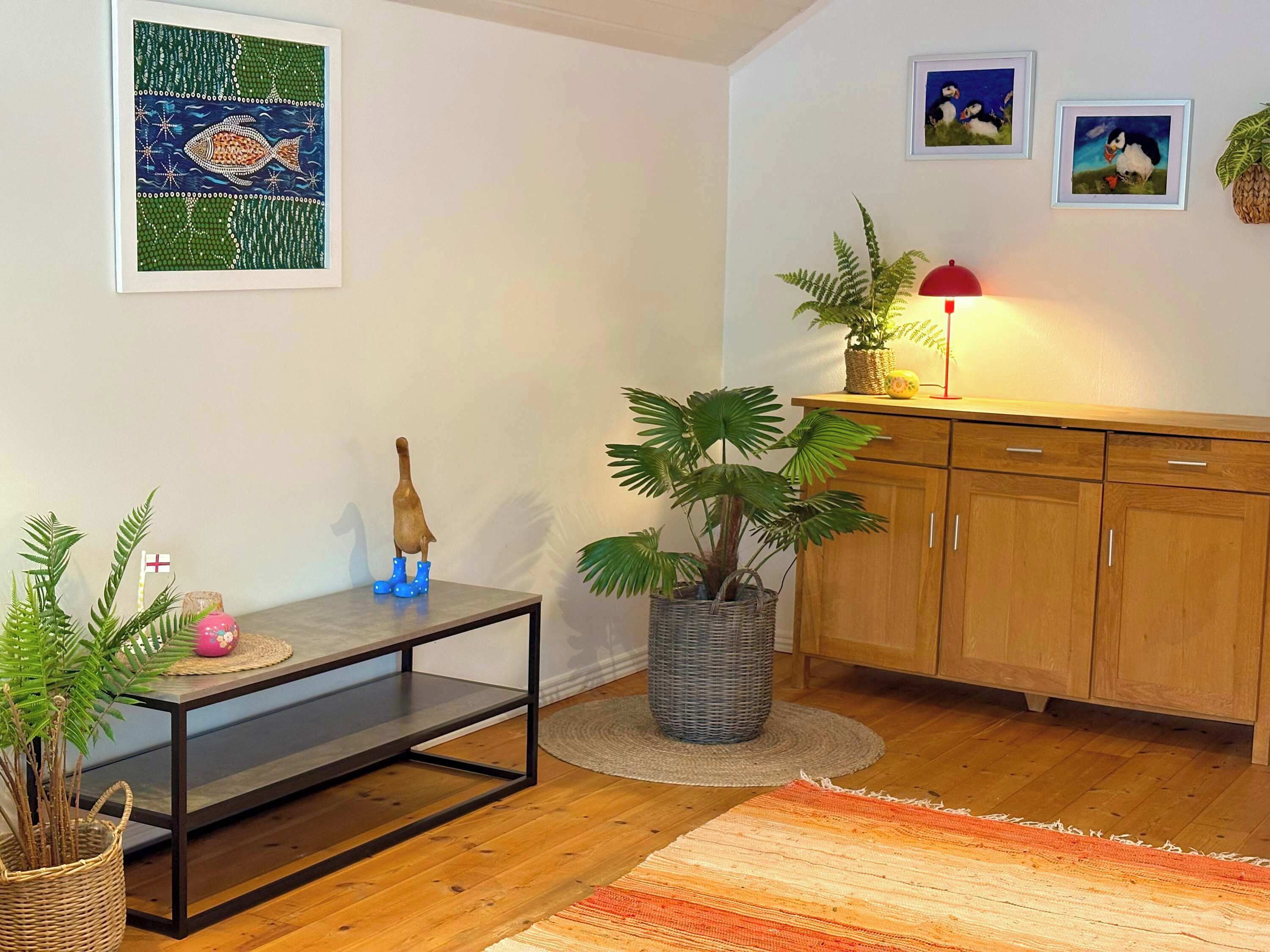 Un salon avec un plancher en bois, une table à manger agrémentée d’une plante, un meuble et des œuvres d’art encadrées accrochées au mur.
