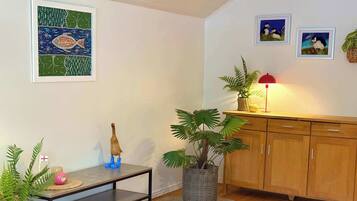 A living room with a wooden floor, a dining table with a plant, a cabinet, and framed artwork on the wall.